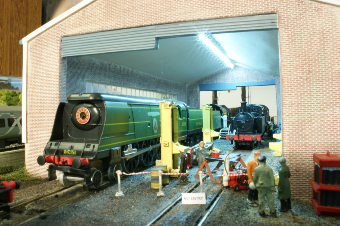 Image showing two model steam trains in a railway workshop which looks real but is actually a scale model.