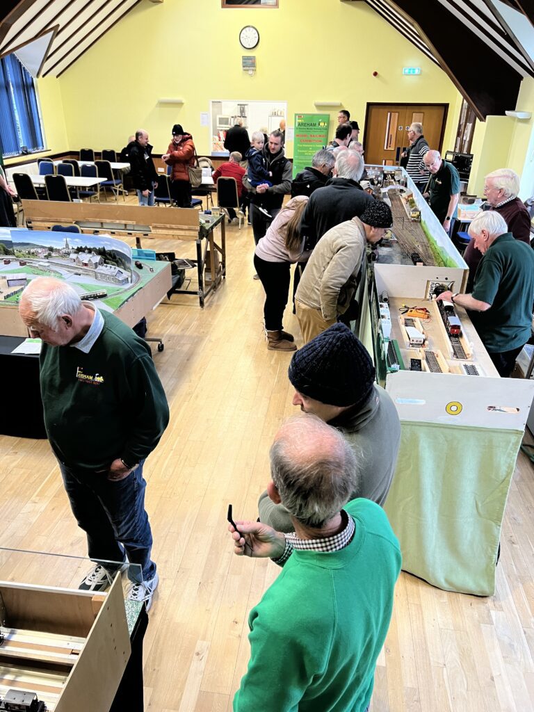 Image shows several layouts on display in Portchester Parish Halls with people of all ages observing the layouts. 